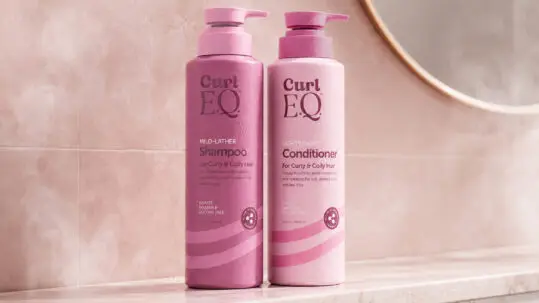 Read the article: What Makes a Good Formula for Curly Hair? Image: CurlEQ shampoo and conditioner bottles displayed on a bathroom counter beside a mirror