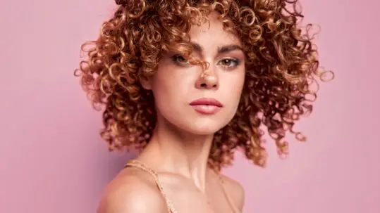 Read the article: How to Manage Frizzy Curly Hair Image: Smiling model with nice short light brown curly hair