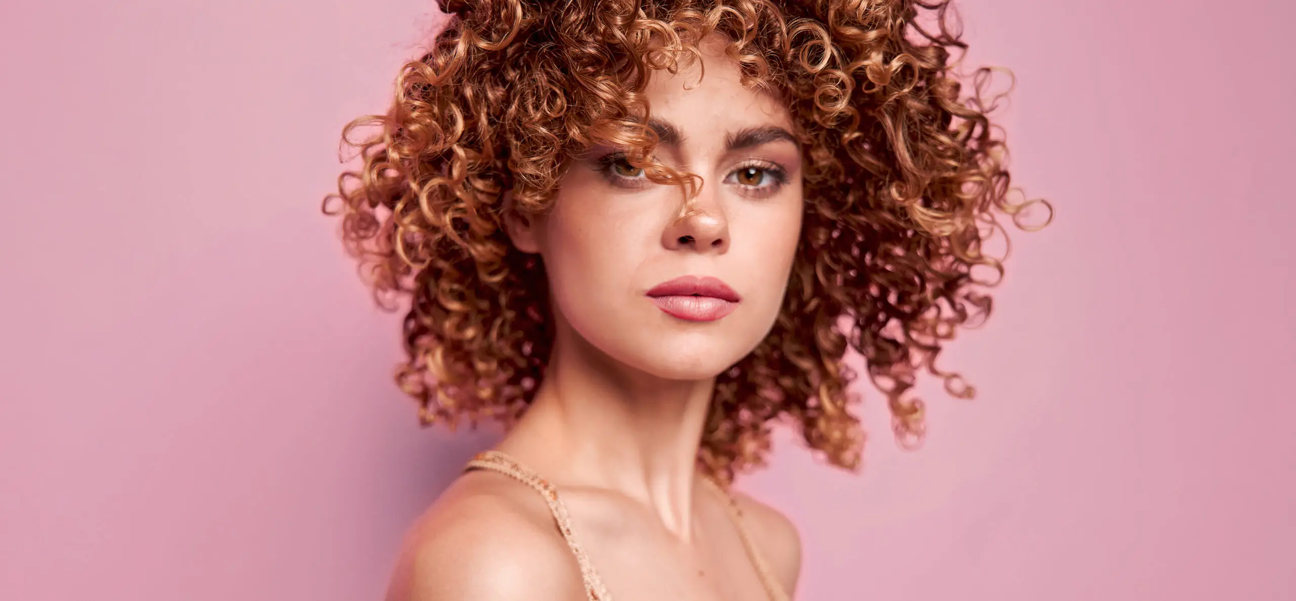 Read the article: How to Manage Frizzy Curly Hair Image: Smiling model with nice short light brown curly hair