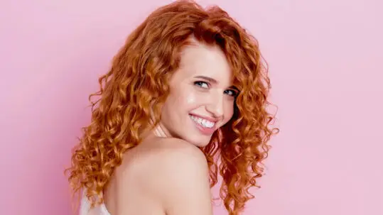 Read the article:Refreshing Curls Between Wash Days Image: Smiling model with curly copper color hair
